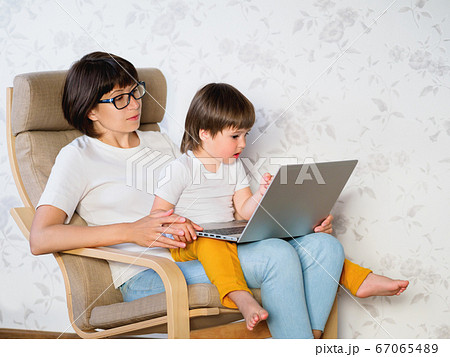 Mother and her toddler boy sit together on chair with laptop. Woman tries to remote work, but kid is asking for game or cartoons. quarantine lockdown because of coronavirus COVID-19. Mother and her toddler boy sit together on chair with laptop. Woman tries to remote work, but kid is asking for game or cartoons. quarantine lockdown because of coronavirus COVID-19. 67065489