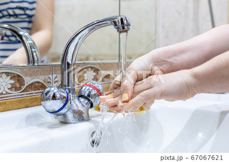 The girl washes her hands with soap under the tap with water. Personal hygiene. Disinfection. Hygiene concept. Corona virus Prevention to stop spreading coronavirus. The girl washes her hands with soap under the tap with water. Personal hygiene. Disinfection. Hygiene concept. Corona virus Prevention to stop spreading coronavirus. 67067621