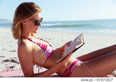 Woman reading a book while laying on the beach 67071927
