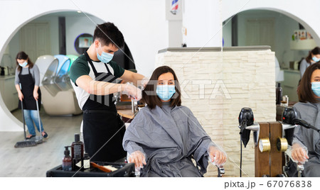 Young man professional hairdresser in mask cut female's hair Young man professional hairdresser in mask cut female's hair 67076838