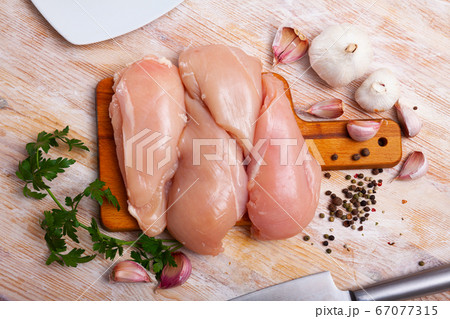 Preparation of raw chicken breast fillet with parsley and garlic on cutting board 67077315