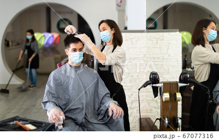 Client in mask during hair cut by professional hairdresser in mask Client in mask during hair cut by professional hairdresser in mask 67077316