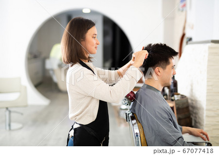 Woman doing haircut for man in salon 67077418