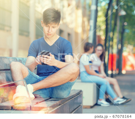Teenager is typing message on smartphone while sitting on bench Teenager is typing message on smartphone while sitting on bench 67078164
