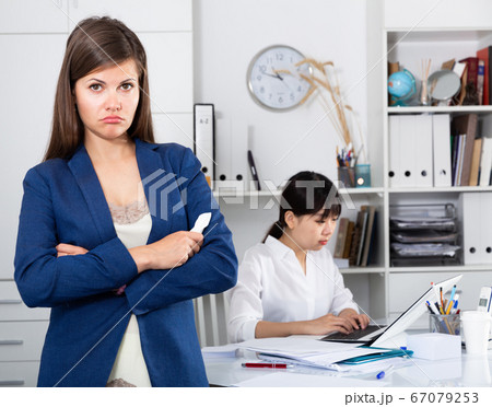 Business woman crying standing in office with working colleague behind 67079253