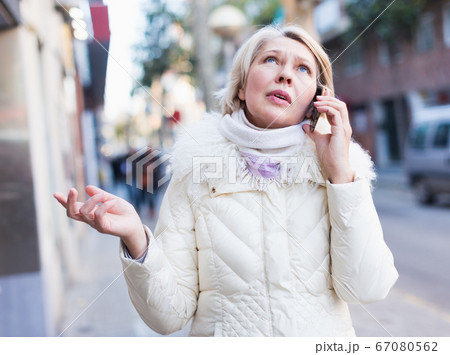Mature woman is talking by phone in time walking 67080562