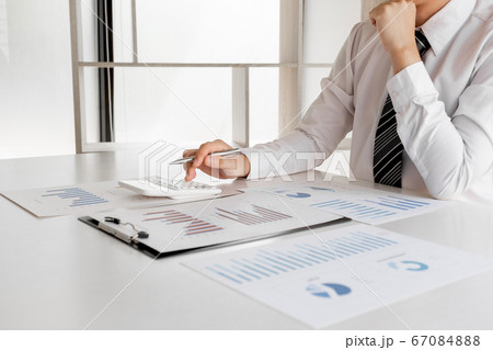 A businessman is sitting at a desk and calculating financial graphs about real estate investment expenditures A businessman is sitting at a desk and calculating financial graphs about real estate investment expenditures 67084888
