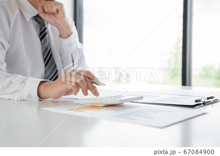 A businessman is sitting at a desk and calculating financial graphs about real estate investment expenditures 67084900