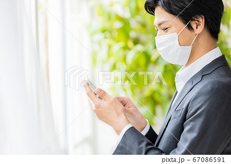スマホを操作するマスクをつけた若い男性 スマホを操作するマスクをつけた若い男性 67086591
