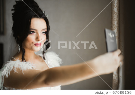 A sweet smiling bride in a light interior makes selfie on the phone 67089156