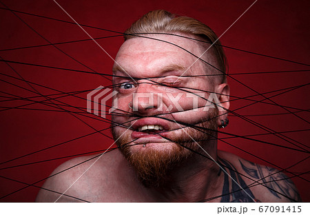 Portrait of tangled in black threads blond man on red background 67091415