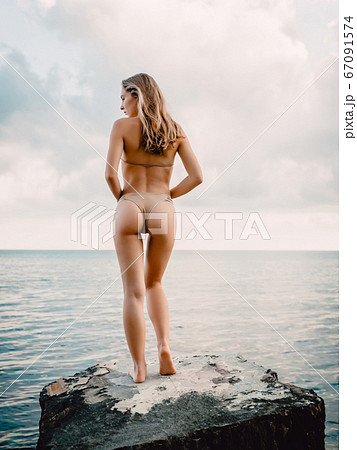 Young attractive woman in bikini posing at stones. Slim girl at sea Young attractive woman in bikini posing at stones. Slim girl at sea 67091574