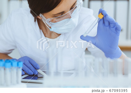 Close-up of professional female scientist in protective eyeglasses making experiment with reagents in laboratory. Medicine and research concept Close-up of professional female scientist in protective eyeglasses making experiment with reagents in laboratory. Medicine and research concept 67093395