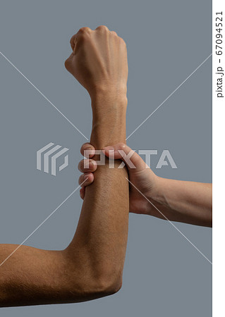 Close-up of light-skinned hand clenching dark-skinned forearm 67094521