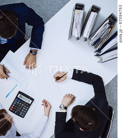 Business people at meeting, view from above. Bookkeeper or financial inspector making report, calculating or checking balance Business people at meeting, view from above. Bookkeeper or financial inspector making report, calculating or checking balance 67094763