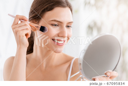 Smiling woman applying blush on face with brush tool 67095834