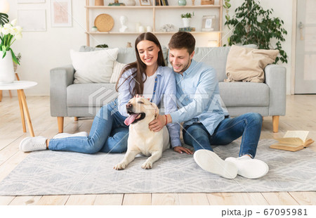 Young happy couple with dog sitting in living room 67095981