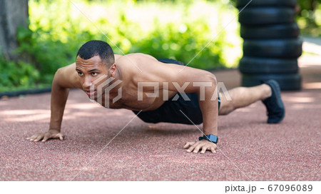 Shirtless muscular black guy performing push ups on jogging track at city park Shirtless muscular black guy performing push ups on jogging track at city park 67096089