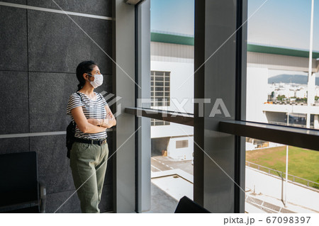 Young woman is standing in a waiting hall with a protection mask. Corona virus outbreaking. 67098397