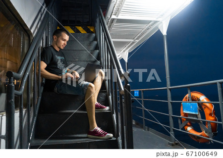 A young man works on a laptop on the deck of a 67100649