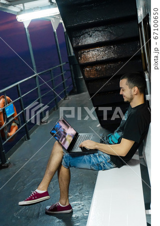 A young man works on a laptop on the deck of a 67100650