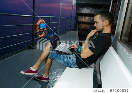 A young man works on a laptop on the deck of a 67100651