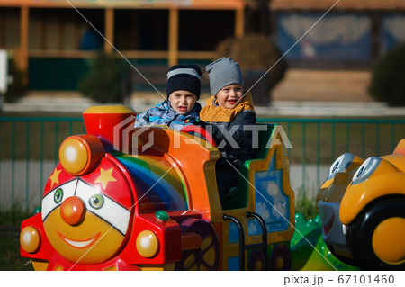 Children's rest in the amusement park. Two boys ride a children's colored locomotive by rail. Happy 67101460