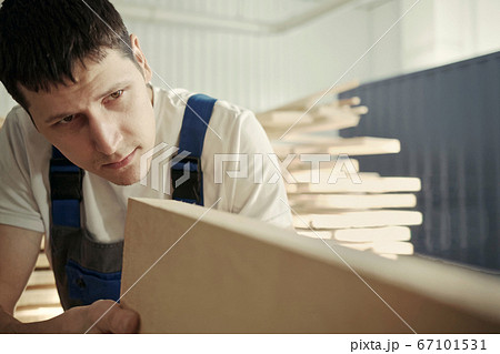 A young carpenter chooses a wooden board. Inspection and quality control of wood. Worker in the A young carpenter chooses a wooden board. Inspection and quality control of wood. Worker in the 67101531