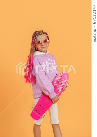 Active young girl in pink shirt and white shorts holding skateboard over yellow background Active young girl in pink shirt and white shorts holding skateboard over yellow background 67122147