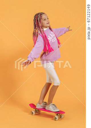 Active young girl in pink shirt and white shorts holding skateboard over yellow background 67122149
