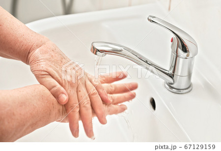 Senior woman washing her hands with soap under tap Senior woman washing her hands with soap under tap 67129159