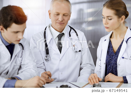 Doctors colleagues and elderly therapist discussing current disease therapy while sitting at working place in sunny clinic. Teamwork in medicine 67149541