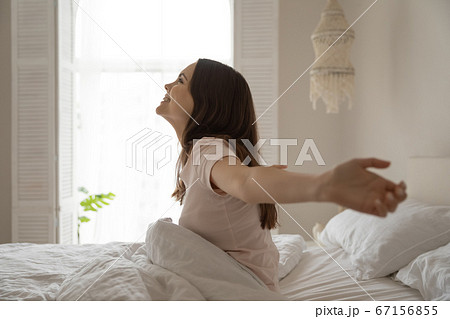 Smiling beautiful woman sitting in bed, stretching after awakening Smiling beautiful woman sitting in bed, stretching after awakening 67156855