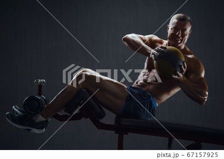 Fitness man pumping up abs muscles in gym Fitness man pumping up abs muscles in gym 67157925