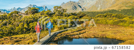 New Zealand Hiking. Panoramic banner of Young hiking couple walking on trail at Routeburn Track during. Hikers carrying backpacks tramping Key Summit Track, Fiordland National Park, New Zealand 67158582