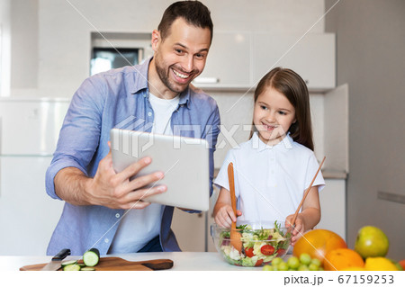 Father And Daughter Using Tablet Cooking In Kitchen At Home 67159253