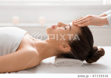 Massage therapist rubbing woman forehead, spa salon interior 67159316