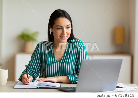 Woman At Laptop Taking Notes Learning Wearing Earbuds In Office 67159319