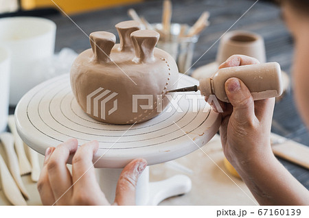 Closeup of bottom of mug, which is being decorated in ceramic studio. Female professional hands making clay dots or drops on the surface of vase by special squeezing tool. Closeup of bottom of mug, which is being decorated in ceramic studio. Female professional hands making clay dots or drops on the surface of vase by special squeezing tool. 67160139