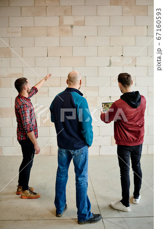 Back view of three young builders or architects discussing quality of bricks 67160593