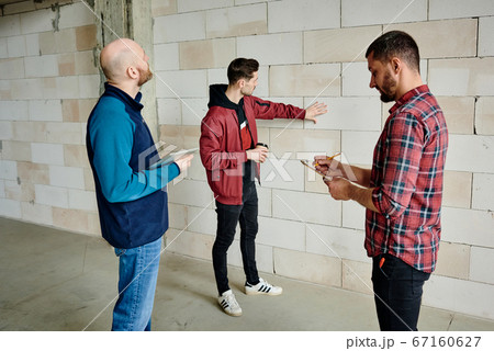 Young contractor with drink touching white brick while standing by wall Young contractor with drink touching white brick while standing by wall 67160627