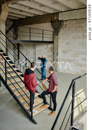 Two young builders in workwear standing on staircase inside unfinished building Two young builders in workwear standing on staircase inside unfinished building 67160638
