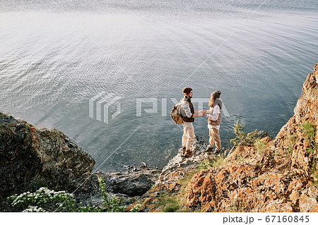Young affectionate romantic couple holding by hands while standing by waterside 67160845