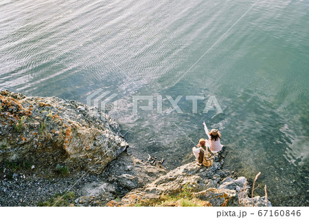 Young female backpacker pointing at far riverbank while sitting by water 67160846