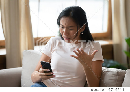 Young vietnamese woman feeling annoyed looking at smartphone screen. 67162114