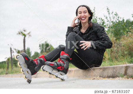 Happy Woman on roller skating pause, sitting on the street and using mobile phone. Pretty, Urban Happy Woman on roller skating pause, sitting on the street and using mobile phone. Pretty, Urban 67163107
