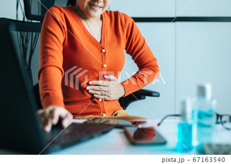 Asian woman having painful stomach ache during working from home,Female suffering from abdominal pain,Period cramps,Hands squeezing belly,Stomach pain 67163540