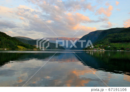 ノルウェー ハダンゲルフィヨルド ウルヴィク地区ホテル南側より白夜の黄昏の山々と夕焼け空と水面を望むの写真素材