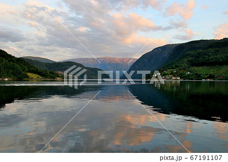 ノルウェー　ハダンゲルフィヨルド、ウルヴィク地区ホテル南側より白夜の黄昏の夕焼け空と水面と山々を望む 67191107