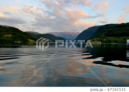 ノルウェー　ハダンゲルフィヨルド、ウルヴィク地区より白夜の黄昏時の山々と水面と空の変化の推移を楽しむ 67191535